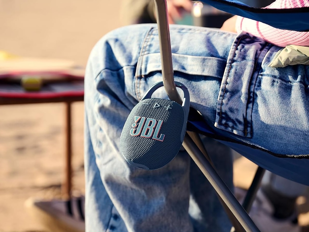 JBL Clip 5 bærbar Bluetooth højttaler fastgjort til en stol ved stranden.